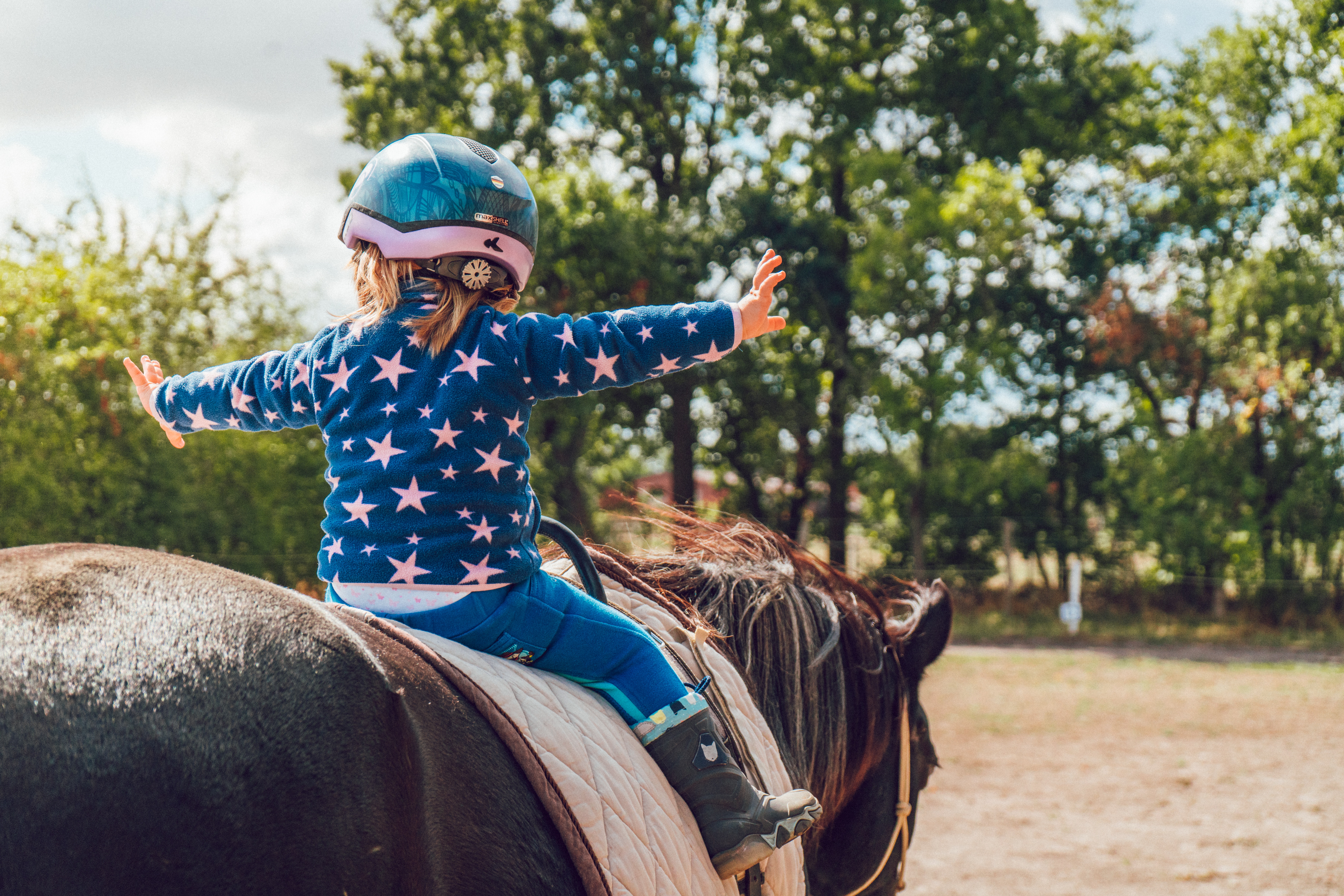 petite fille travaillant son équilibre sur un cheval en séance d'hippothérapie dans le cadre de la thérapie intensive.