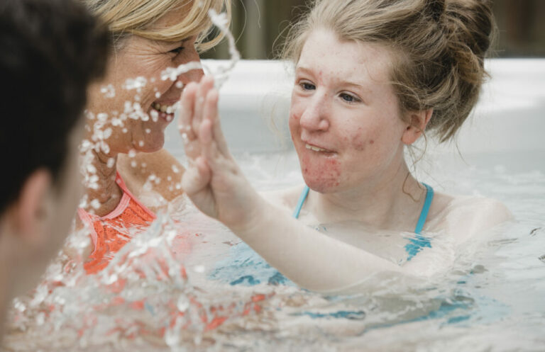 jeune fille atteinte de paralysie cérébrale joyeuse joue dans l'eau du spa avec sa famille