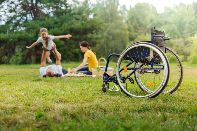 jeune fille atteinte de paralysie cérébrale joyeuse joue avec ses parents dans le parc ICARE Center en délaissant son fauteuil roulant.